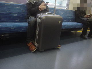 電車内でスーツケースが動かないよう足で押さえてる人